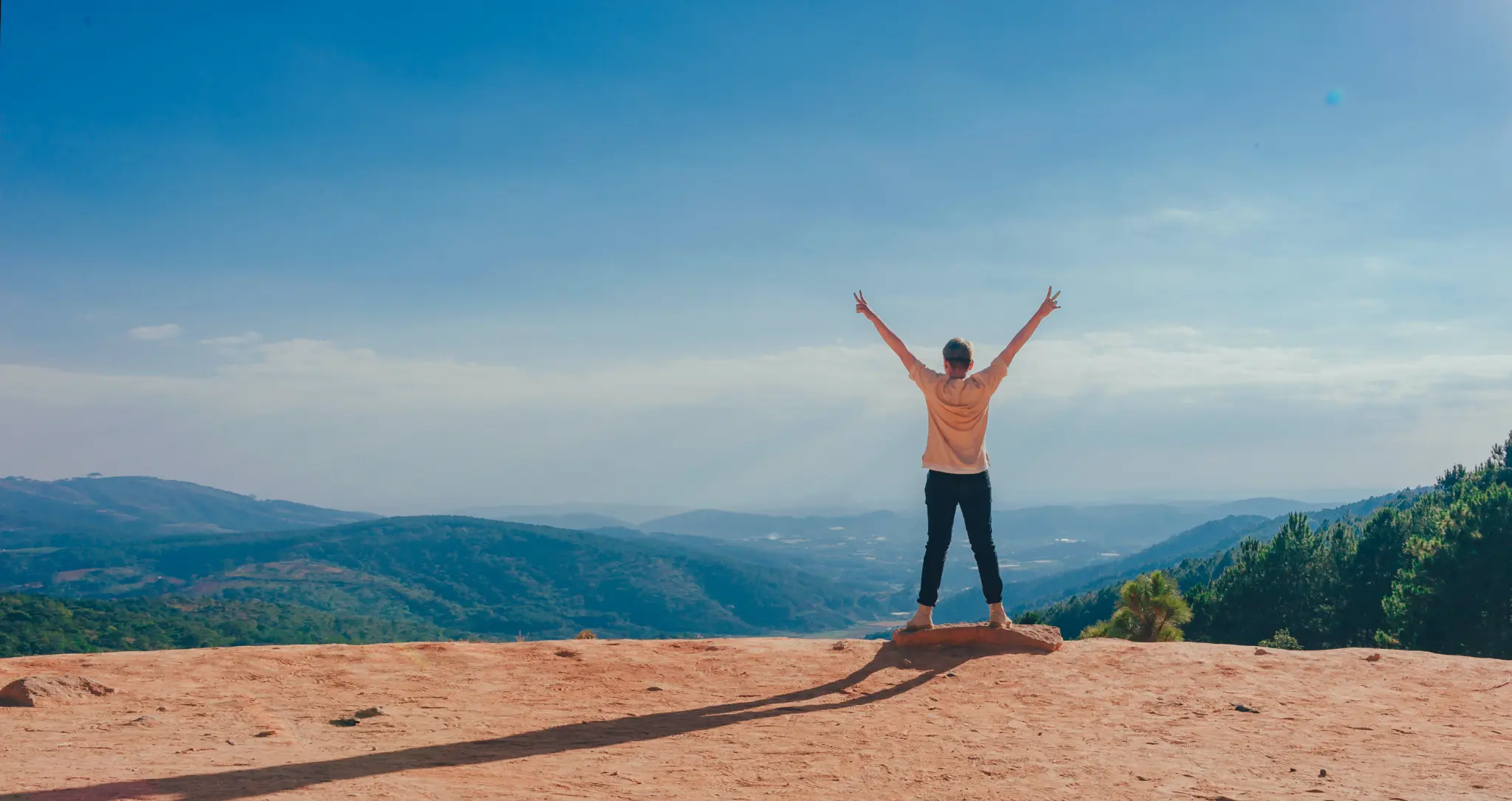 Person standing on a hilltop with arms raised, overlooking a valley — freedom and hope
