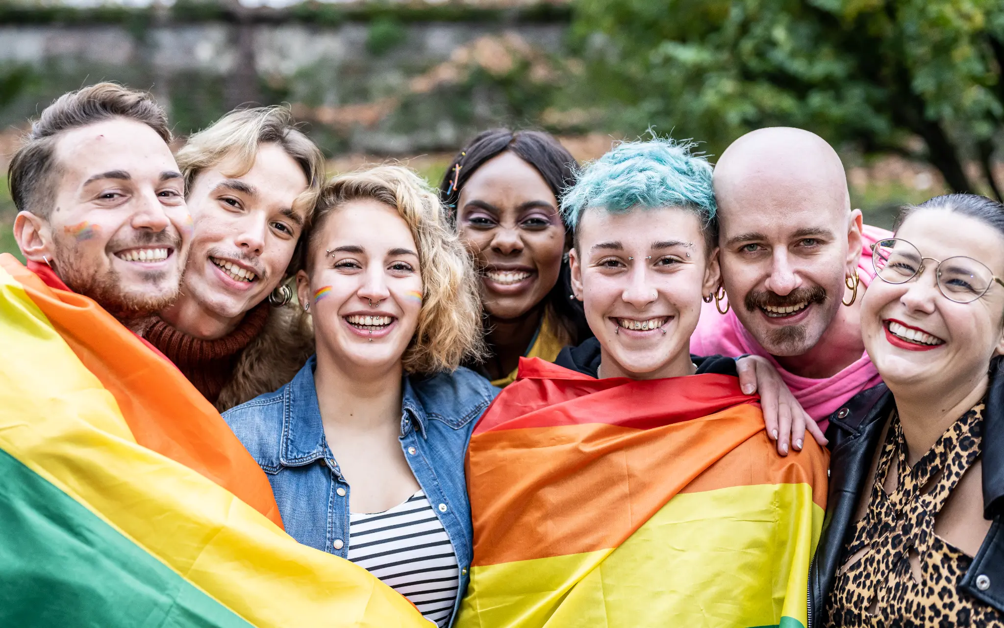Diverse group of LGBTQ friends smiling together with rainbow flag